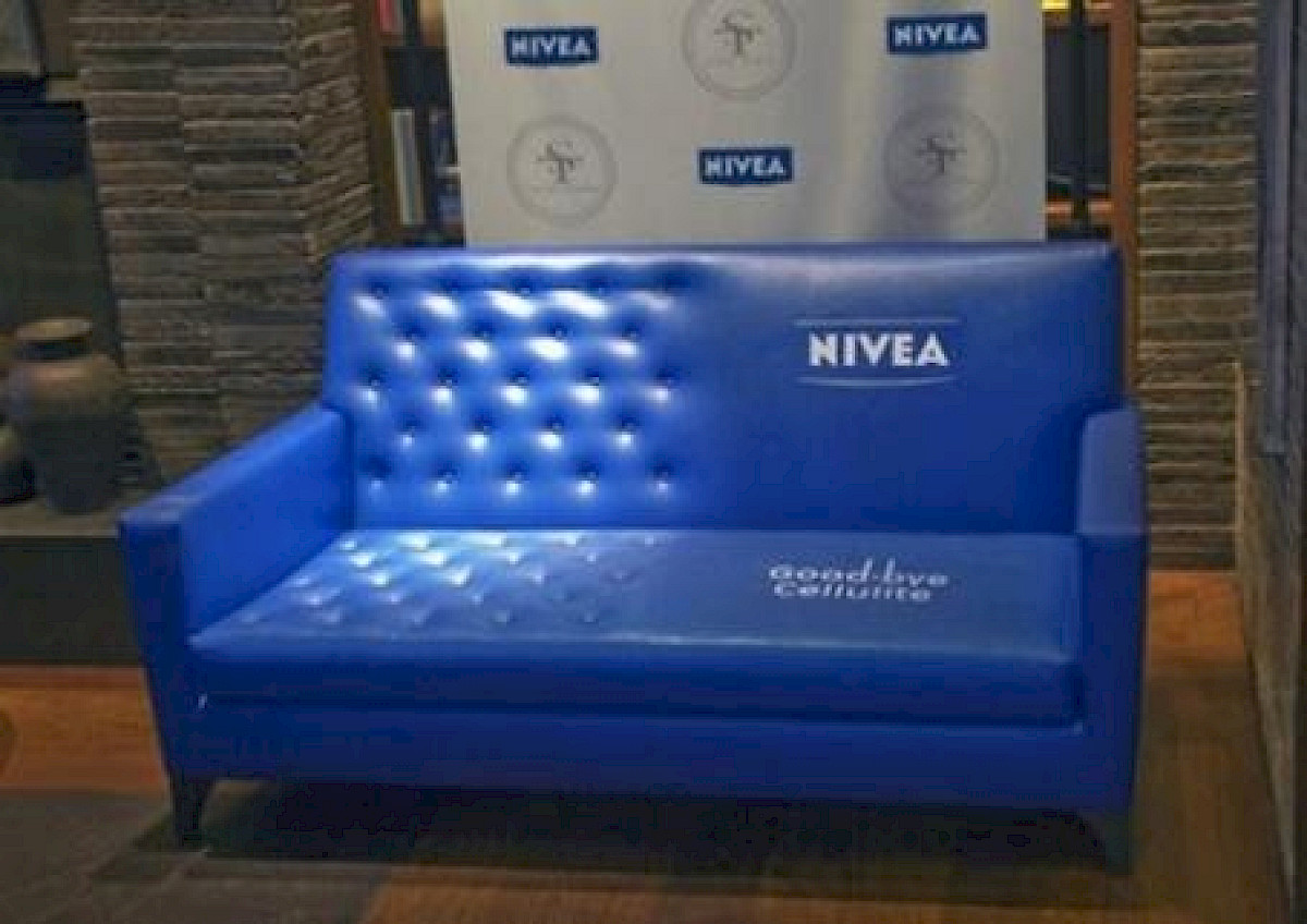 Modrý gauč, na polovině hladký s logem NIVEA a textem Goodbye cellulite, na druhé půlce prošívaný