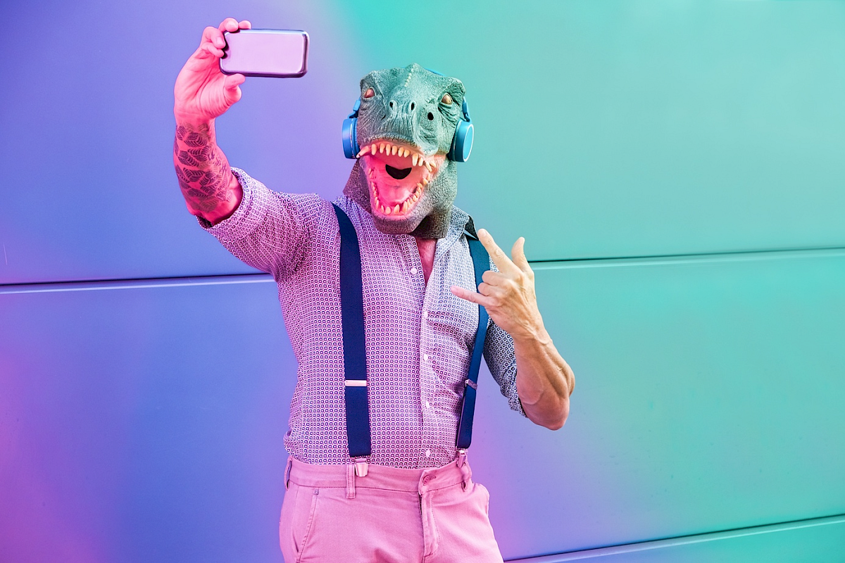 Muž s maskou dinosaura dělající selfie